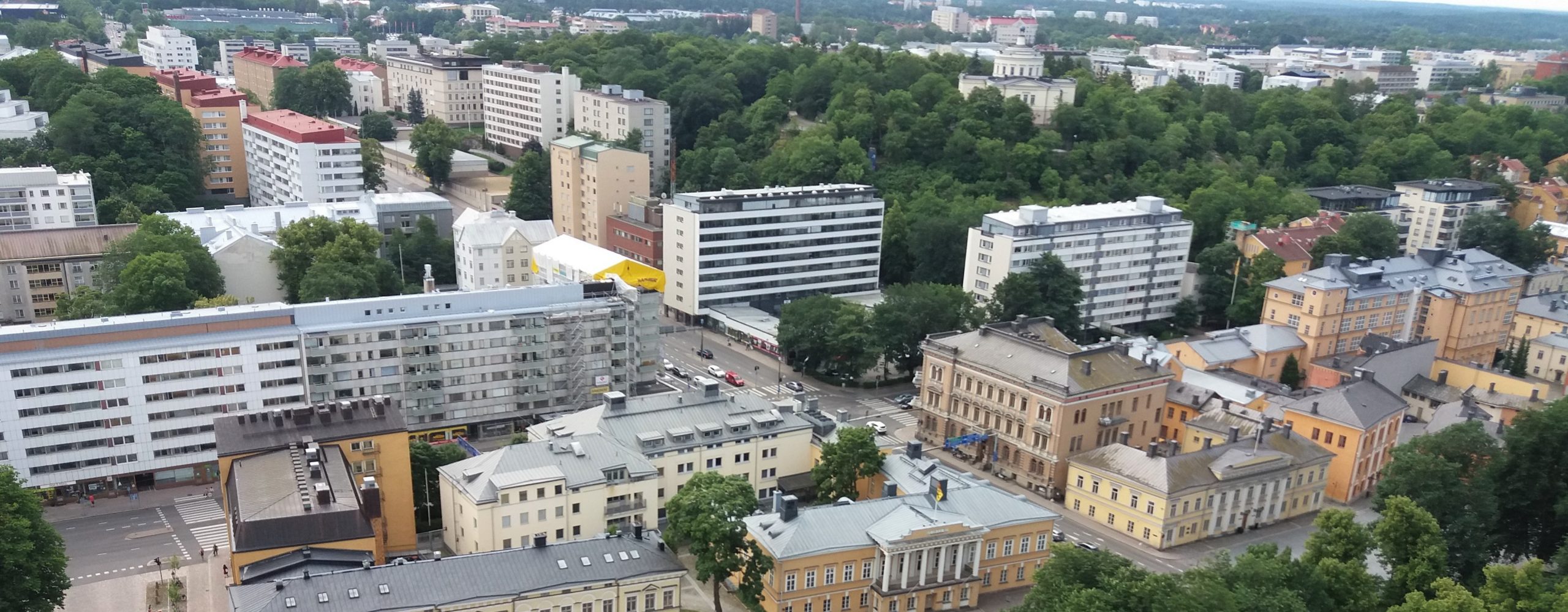 Kuvassa näkyy Turun eteläinen keskusta. Etualalla tuomiokirkon vieressä rakennuskanta on vanhinta ja matalinta. Kuvassa on paljon valkoisia, vaaleita ja beigejä kerrostaloja monelta eri vuosikymmeneltä.