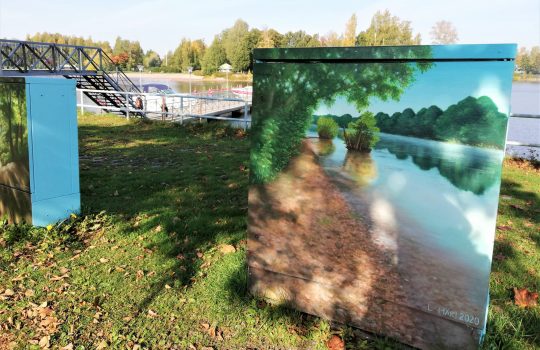 Kuvassa sähkölaatikossa maalaus jokimaisemasta. Taustalla näkyy Kokemäenjoki ja Kirjurinluotoon johtava kävelysilta.