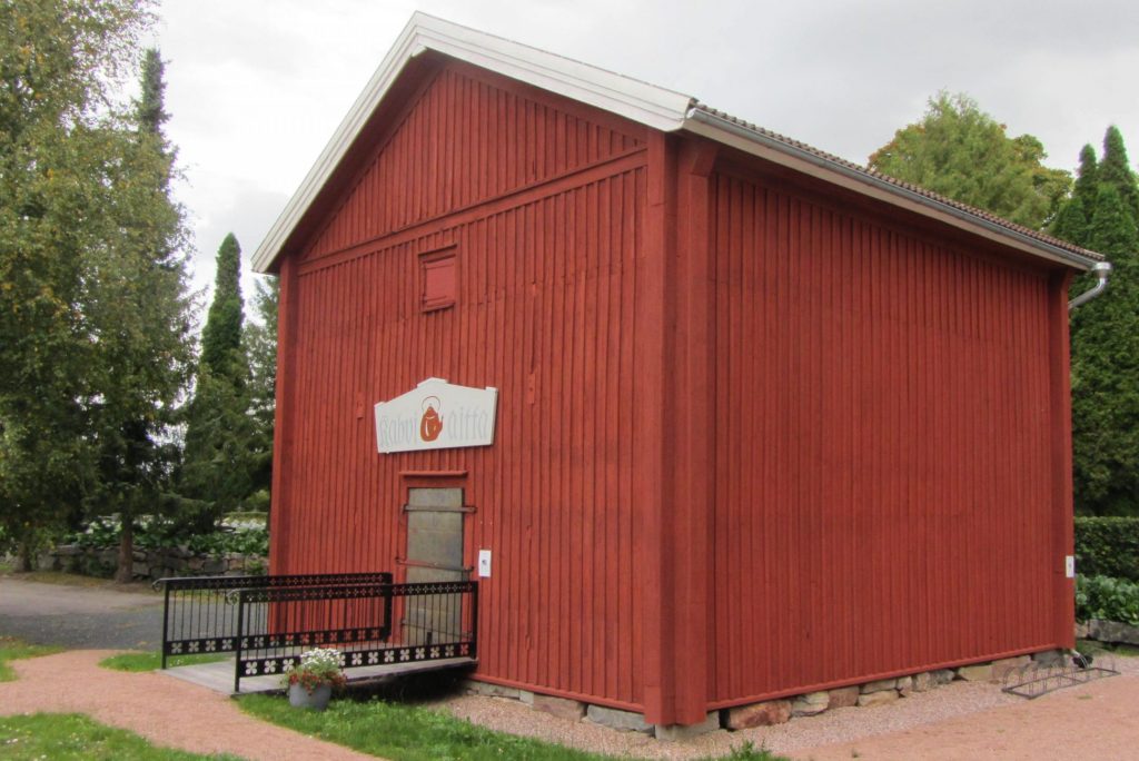 Kuvassa punainen puurakennus, jossa oven yllä kyltti kahviaitta.