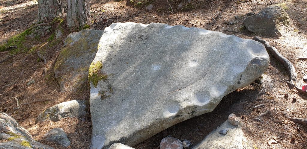 Lähikuvassa iso kolmion mallinen litteä kivi, jonka reunoissa on koloja, joita koputtelemalla kivi soi.
