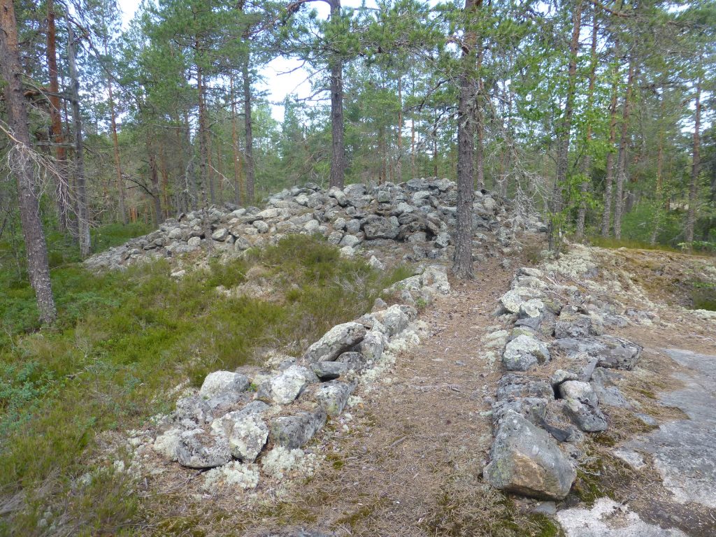 Kuvassa kiviröykkiö eli kivistä muodostunut kasa ja kivien reunaama polku röykkiölle. Ympärillä metsää.