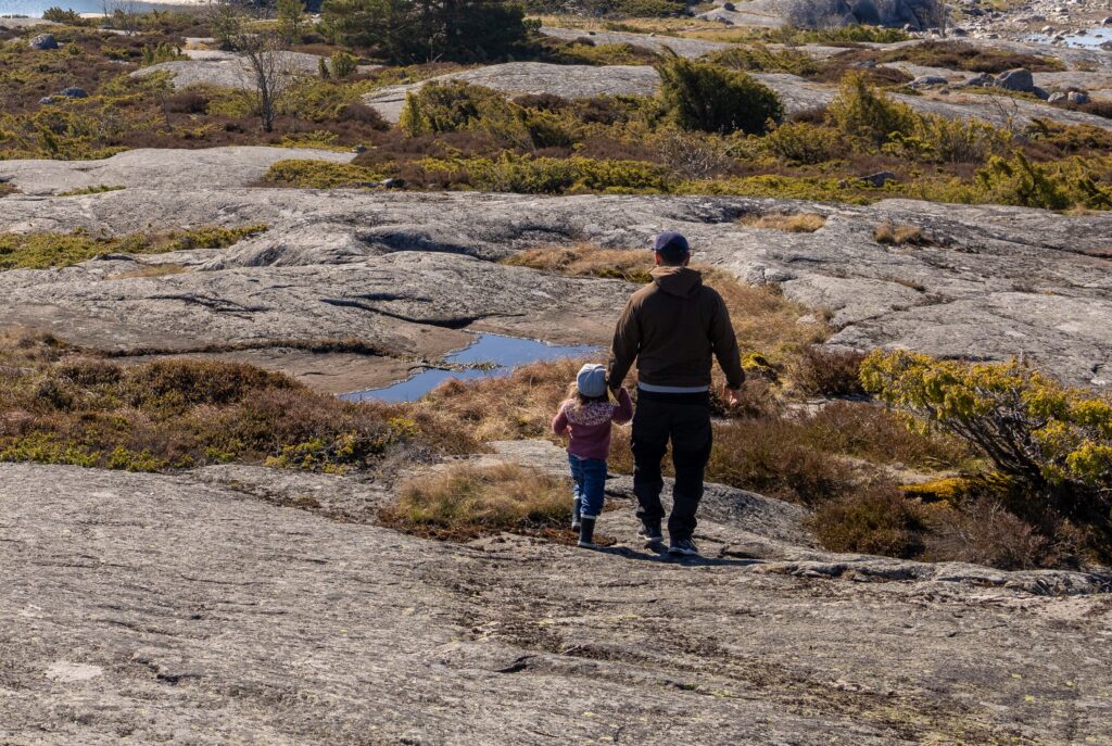 Mies ja pieni tyttö kävelevät rantakalliolla.